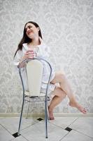 portrait d'une jolie jeune femme en chemise masculine et sous-vêtements assis avec un verre d'eau dans les mains. photo