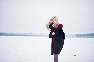 élégance fille blonde en manteau de fourrure et robe de soirée rouge posée au jour de neige d'hiver. photo