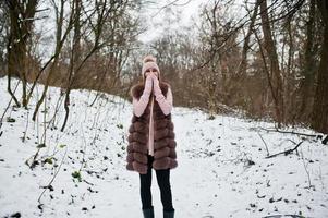 fille élégante en manteau de fourrure et couvre-chef à la forêt d'hiver. photo