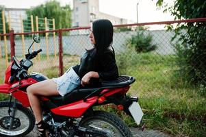 portrait d'une femme cool et géniale en robe et veste en cuir noir assise sur une moto rouge cool. photo