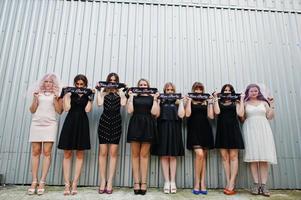 groupe de 8 filles portant du noir et 2 mariées à la fête de poule posées contre un mur en acier. photo