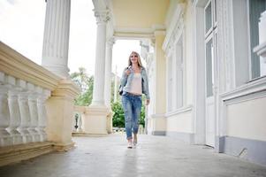 fille blonde porte un jean avec sac à dos posé contre une maison vintage. photo