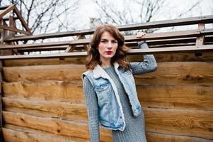 portrait de fille brune bouclée en veste de jeans contre le mur en bois. photo