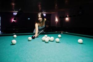 portrait d'une jolie jeune femme en robe jouant au billard. photo