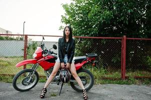 portrait d'une femme cool et géniale en robe et veste en cuir noir assise sur une moto rouge cool. photo