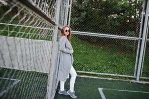 fille en manteau gris avec des lunettes de soleil au petit stade de rue. photo