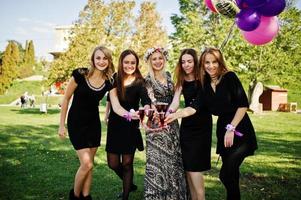 cinq filles portent du noir avec des ballons buvant du champagne rouge à la fête de poule. photo