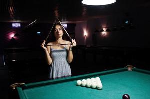 portrait d'une femme confuse posant avec un triangle au bord de la table de billard. photo