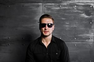 portrait en studio d'un homme élégant portant une chemise noire et des lunettes contre un mur en acier. photo