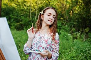 portrait d'une jolie jeune femme en robe longue peignant à l'aquarelle dans la nature. photo