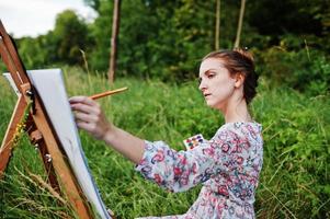 portrait d'une magnifique jeune femme heureuse en belle robe assise sur l'herbe et peinture sur papier à l'aquarelle. photo