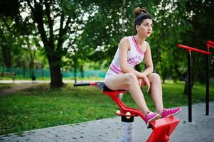 fille de sport porter sur un short blanc et une chemise faisant des exercices sur des simulateurs en plein air au parc. photo