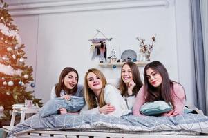 quatre amies mignonnes que les filles portent sur des chandails chauds et un pantalon noir sur le lit dans la chambre décorée du nouvel an en studio, jouent avec des oreillers. photo