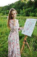 portrait d'une jolie jeune femme en robe longue peignant à l'aquarelle dans la nature. photo