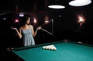 portrait d'une femme confuse posant avec un triangle au bord de la table de billard. photo