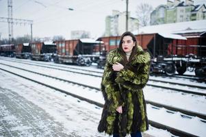 fille brune en manteau de fourrure vert sur la station de plate-forme à la journée d'hiver. photo