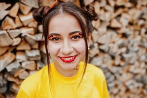 jeune fille drôle avec un maquillage lumineux, porter sur une chemise jaune sur fond en bois. photo