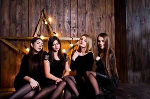 quatre amies mignonnes filles portent des robes noires contre une grande décoration d'étoile de noël lumineuse sur fond en bois. photo