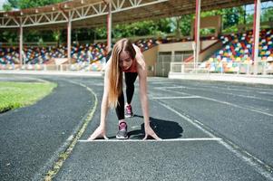 fitness fille sportive en tenue de sport au stade sports de plein air. heureuse femme sexy qui court sur un tapis roulant de piste d'athlétisme sur le stade. photo