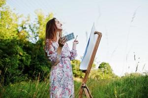 portrait d'une jolie jeune femme en robe longue peignant à l'aquarelle dans la nature. photo