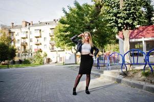 fille blonde élégante portant une veste en cuir noir posant dans les rues de la ville. photo