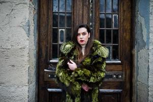 fille brune en manteau de fourrure vert contre de vieilles portes en bois. photo