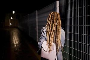 fille avec des dreadlocks marchant dans la rue de nuit de la ville. photo