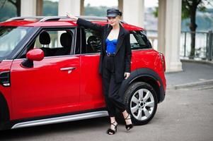 portrait d'une belle mannequin blonde sexy en casquette et en corset noir et bleu, avec un maquillage lumineux près d'une voiture de ville rouge. photo