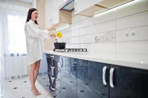 fille brune, porter une chemise et des sous-vêtements cuisinant à la cuisine blanche. photo