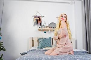 fille blonde élégante portant une tunique chaude assise sur le lit. photo