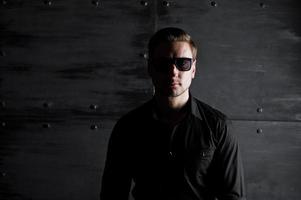 portrait en studio d'un homme élégant portant une chemise noire et des lunettes contre un mur en acier. photo