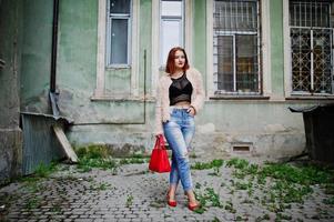 fille aux cheveux rouges avec sac à main rouge posé dans la rue de la ville. photo