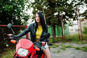 portrait d'une femme cool et géniale en robe et veste en cuir noir assise sur une moto rouge cool. photo