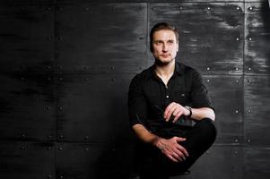 portrait en studio d'un homme élégant portant une chemise noire contre un mur en acier. photo