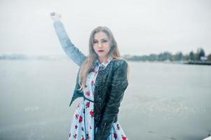 une fille élégante en veste de cuir tient une fusée de fumée rose le jour de l'hiver contre un lac gelé. photo