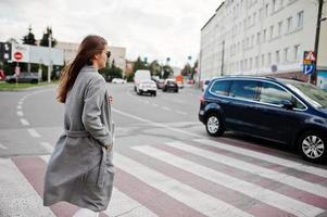 fille en manteau gris avec lunettes de soleil et sac à main marchant sur le passage pour piétons. photo