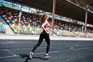 fitness fille sportive en tenue de sport au stade sports de plein air. heureuse femme sexy qui court sur un tapis roulant de piste d'athlétisme sur le stade. photo