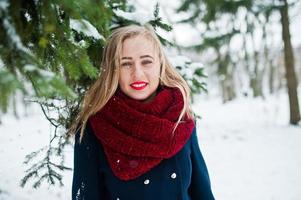 fille blonde en écharpe rouge et manteau marchant au parc le jour de l'hiver. photo