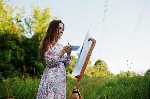 portrait d'une jolie jeune femme en robe longue peignant à l'aquarelle dans la nature. photo