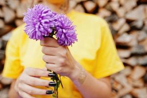 fleurs d'aster violet aux mains d'une fille en chemise jaune. photo