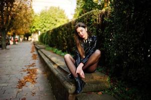 fille brune élégante porte une veste en cuir et un short assis dans la rue de la ville d'automne. photo