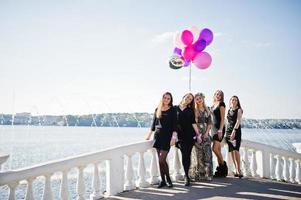 cinq filles portent du noir marchant avec des ballons lors d'une fête de poule contre le lac. photo