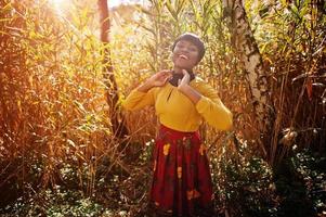 fille afro-américaine en robe jaune et rouge au parc d'automne doré. photo