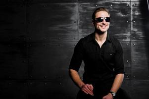 portrait en studio d'un homme élégant portant une chemise noire et des lunettes contre un mur en acier. photo