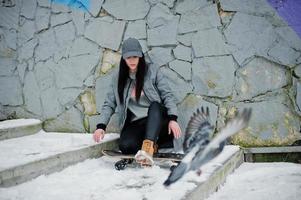 fille brune élégante en casquette grise, style de rue décontracté avec planche à roulettes le jour de l'hiver contre un mur coloré. photo