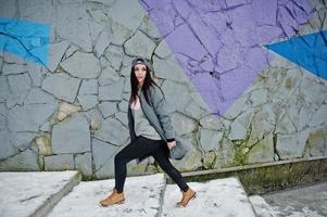 fille brune élégante en casquette grise, style de rue décontracté le jour de l'hiver contre un mur coloré. photo