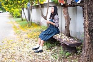 jeune fille assise sur un banc lisant un livre sous un bel arbre. photo