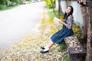 jeune fille assise sur un banc lisant un livre sous un bel arbre. photo