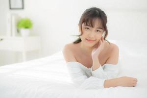 beau portrait jeune femme asiatique allongée et souriante au réveil avec le lever du soleil le matin, beauté jolie fille heureuse et joyeuse reposant sur le lit dans la chambre, mode de vie et concept de détente. photo