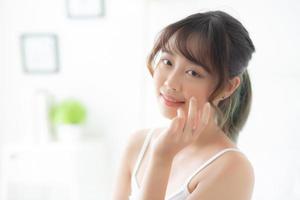 beau portrait femme asiatique maquillage de cosmétique, fille main toucher joue et sourire attrayant, beauté du visage parfaite avec bien-être dans la chambre avec concept de soins de la peau et de soins de santé. photo